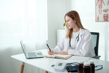 A woman doctor is sitting at a desk with a laptop and a notebook