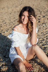 Beautiful slim fashionable woman in white summer dress on the beach by the sea