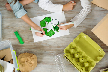 Top view above the painting. Child girl sorts paper and plastic into sorting bin in the kitchen at home.