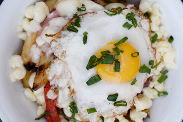 Closeup view of fried potatoes with melted cheese, chorizo, bell pepper, onion and a grilled egg in a white dish.