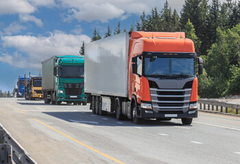 Large trucks move along a country road along the forest