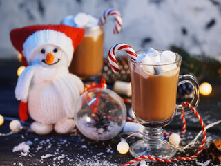 A cup of hot chocolate or cocoa with marshmallows on the table. Christmas decorations, snowman toy.