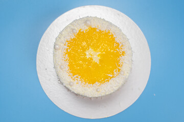 Delicious round yellow cake with orange slice and coconut flakes on blue background