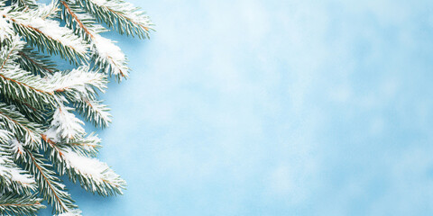 Obraz premium Branch of snowy green spruce, Christmas tree on blue background with snowfall. Winter template, banner flatlay concept for Christmas, New Year and sale season. Web card, backdrop with space for text