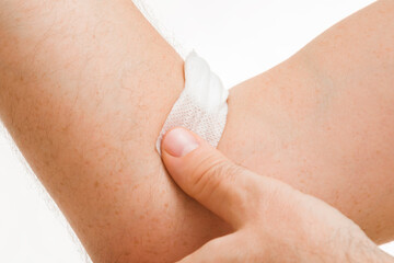 Young adult man gluing and putting bandage with cotton wool on arm vein after blood test on light gray background. Closeup. Front view.
