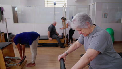 Senior woman exercising with Pilates Machine in physiotherapy group session. Older People taking care of spine health
