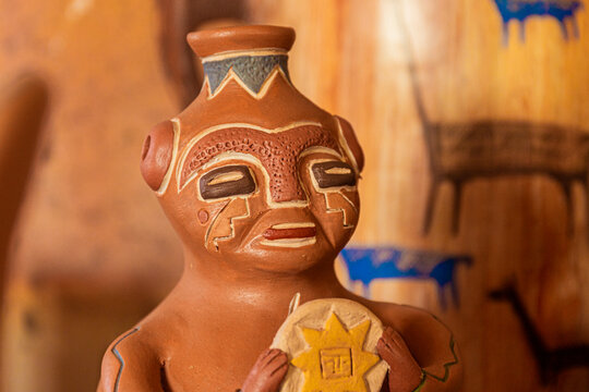 Ceramic figure inspired by pre-Columbian art, with facial details and hand-painted symbols, holding a solar emblem.