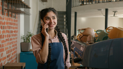 Indian woman waitress barista in apron wipe dust using cleaning duster arabian smiling female girl cleaner bar employee wiping washing shelf with spices in cafe restaurant clean shelves in cafeteria