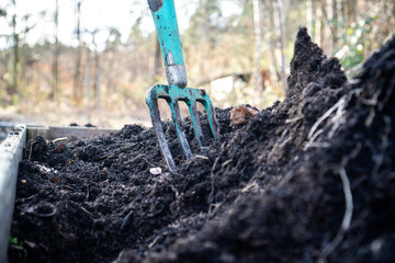 Close-up of a pitchfork in a raised garden bed filled with rich black compost and terra preta (biochar) / Concept: vegetable gardening in spring and fall 