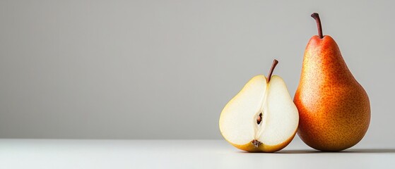 A whole pear and half a pear sit on a white table against a gray background. © ECLIVN