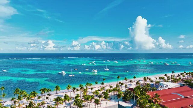 Blue ocean surface at tropical island with lush green palm trees on resort beach. Summer vacation at equator. Palm trees in Caribbean landscape. White clouds over blue sea with white yachts.