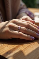Obraz premium Close-up of a Woman's Hand with a Silver Ring Featuring an Amethyst Gemstone on a Wooden Table