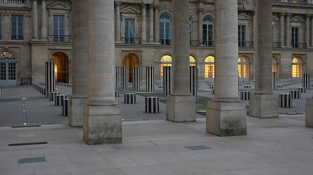 View of the striped art columns at Palais Royal's courtyard, framed by historic colonnades and softly illuminated arched windows at dusk.