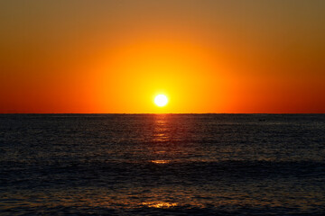 Vibrant Sunset Over Calm Ocean Horizon. A vibrant sunset with a glowing orange sky over a calm ocean horizon, capturing a serene and tranquil seascape.

