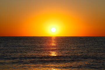 Vibrant Sunset Over Calm Ocean Horizon. A vibrant sunset with a glowing orange sky over a calm ocean horizon, capturing a serene and tranquil seascape.

