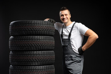 Mechanic leaning on stack of new winter tires posing on black background