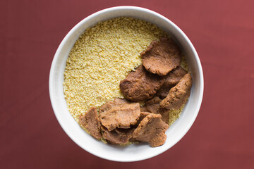 Overhead view of kuli-kuli and yellow garri in a white bowl, top view of nigerian groundnut cakes and garri in a bowl, fresh homemade nigerian kulikuli and cassava in a ceramic bowl
