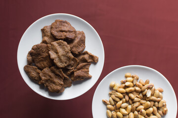 Overhead view of kuli-kuli and roasted peanuts on a white plate, top view of nigerian groundnut cakes and groundnuts on a plate