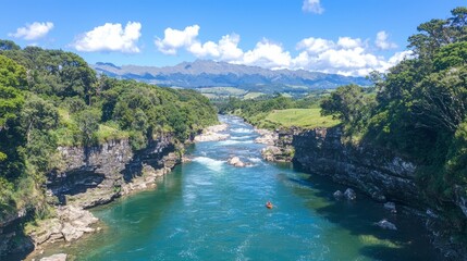 A scenic river flowing through lush greenery and mountains under a blue sky.