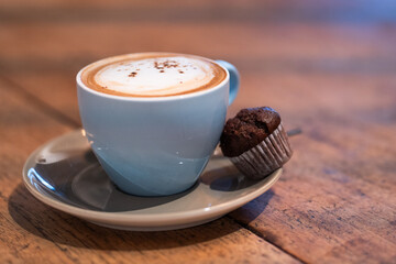 A creamy cappuccino with thick foam and a chocolate muffin, set on a saucer. This still-life composition captures the indulgence of a hot coffee drink paired with a light dessert.