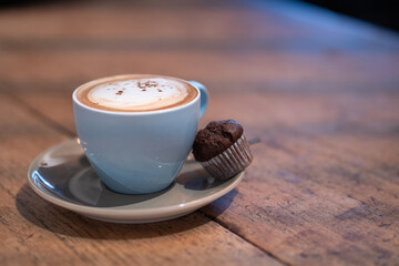 A creamy cappuccino with thick foam and a chocolate muffin, set on a saucer. This still-life composition captures the indulgence of a hot coffee drink paired with a light dessert.