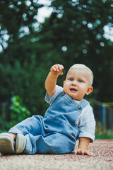 A one-year-old blond boy in a t-shirt and denim dungarees walks in the fresh air. Self-development of the child.