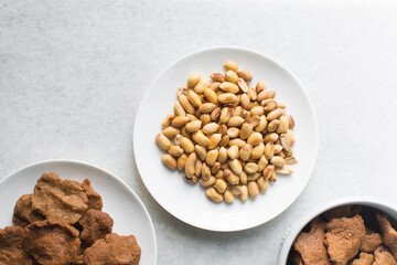 Overhead view of kuli-kuli and roasted peanuts on a white plate, top view of nigerian groundnut cakes and groundnuts on a plate