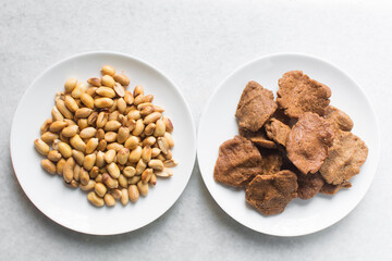 Overhead view of kuli-kuli and roasted peanuts on a white plate, top view of nigerian groundnut cakes and groundnuts on a plate