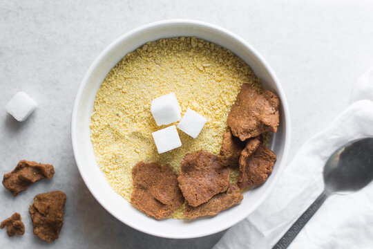 Overhead view of kuli-kuli and yellow garri in a white bowl, top view of nigerian groundnut cakes and garri in a bowl, fresh homemade nigerian kulikuli and cassava in a ceramic bowl