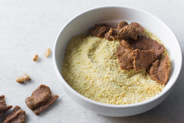 Overhead view of kuli-kuli and yellow garri in a white bowl, top view of nigerian groundnut cakes and garri in a bowl, fresh homemade nigerian kulikuli and cassava in a ceramic bowl