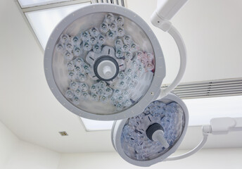 A bright hospital operating room with overhead lights illuminating the sterile environment. The lights are focused, creating an intense, clinical atmosphere for precision surgery