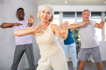 Enthusiastic senior woman practicing hip-hop movements during adult group dance class in studio