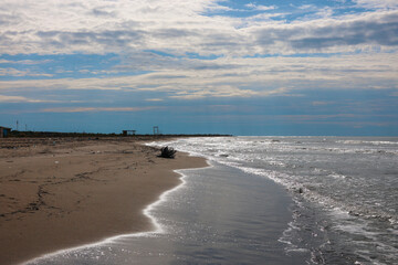 Deserted sandy beach in Albania off-season without people and visitors, with only sea waves, cumulus clouds and a lonely tree branch on the sand of the beach