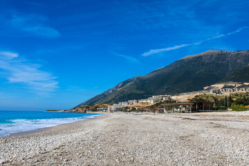 wide pebble beach of Palasës on the Albanian Riviera, deserted outside the tourist season, in the background an apartment complex being built, the Logar Pass and the hilltops of the Logar National Par