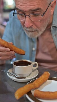 Elderly man with Parkinson's enjoying churros and chocolate, savoring a moment of indulgence