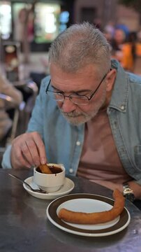 Elderly man with Parkinson's enjoying churros and chocolate, savoring a moment of indulgence
