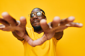 Black man reaching out in yellow shirt, cheerful expression, wearing glasses, vibrant yellow...