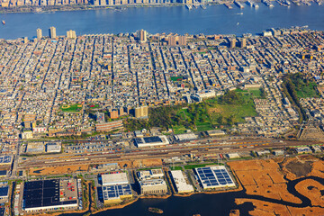 Aerial view of urban area in New Jersey near the Hudson River, featuring buildings, parks, and industrial zones.