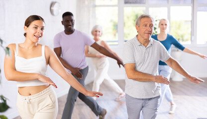 Young woman teacher teaches group of multiethnic mature active people dancing classical dance moves in studio