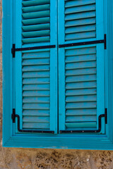 Vibrant blue shutters against rustic stone wall in a sunlit Mediterranean village