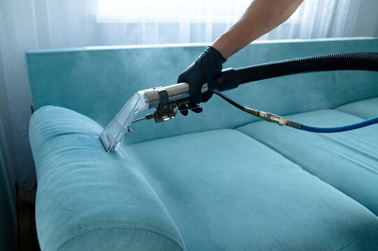Cleaning concept. Man cleans sofa in the room. Virus prevention sanitizing inside. Process of deep furniture cleaning. Professionally chemical cleaning
