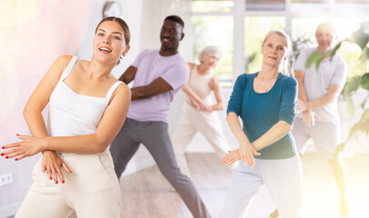 Enthusiastic young girl practicing hip-hop movements during adult group dance class in studio