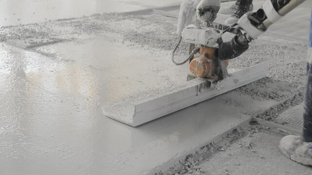 A male worker in a special construction uniform compress concrete surface with a special tool compactor rammer at construction site while performing floor screed. Close up slow motion video