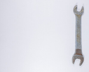 Close-up of a vintage metal spanner with two open ends of different sizes, placed vertically on a white background. The tool shows visible wear and rust, highlighting its rough texture and aged look.

