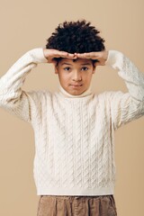 Young african american boy in a white sweater covering his face with his hands, reflecting shyness...