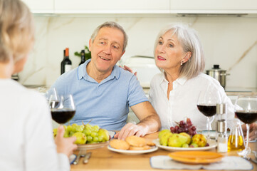 Happy pensioners gathered at the festive table - talking, discussing news and drinking red wine