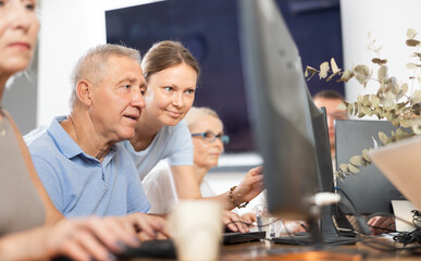 Adult woman teacher teaches group of elderly people to use computer at master class