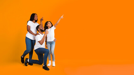 Special Offer. Cheerful African American Family Of Three People Looking Aside And Pointing Fingers Up And Aside At Free Copy Space On Yellow Background, Presenting Empty Place For Advert, Banner