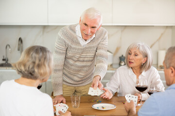 Senior men and women play card game poker during friendly gatherings at home. Couple enthusiastically participate in game, believe in luck, collect chips, distribute winnings