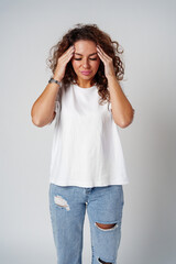 Woman with curly hair holds her head in discomfort, expressing concern or stress in a neutral backdrop